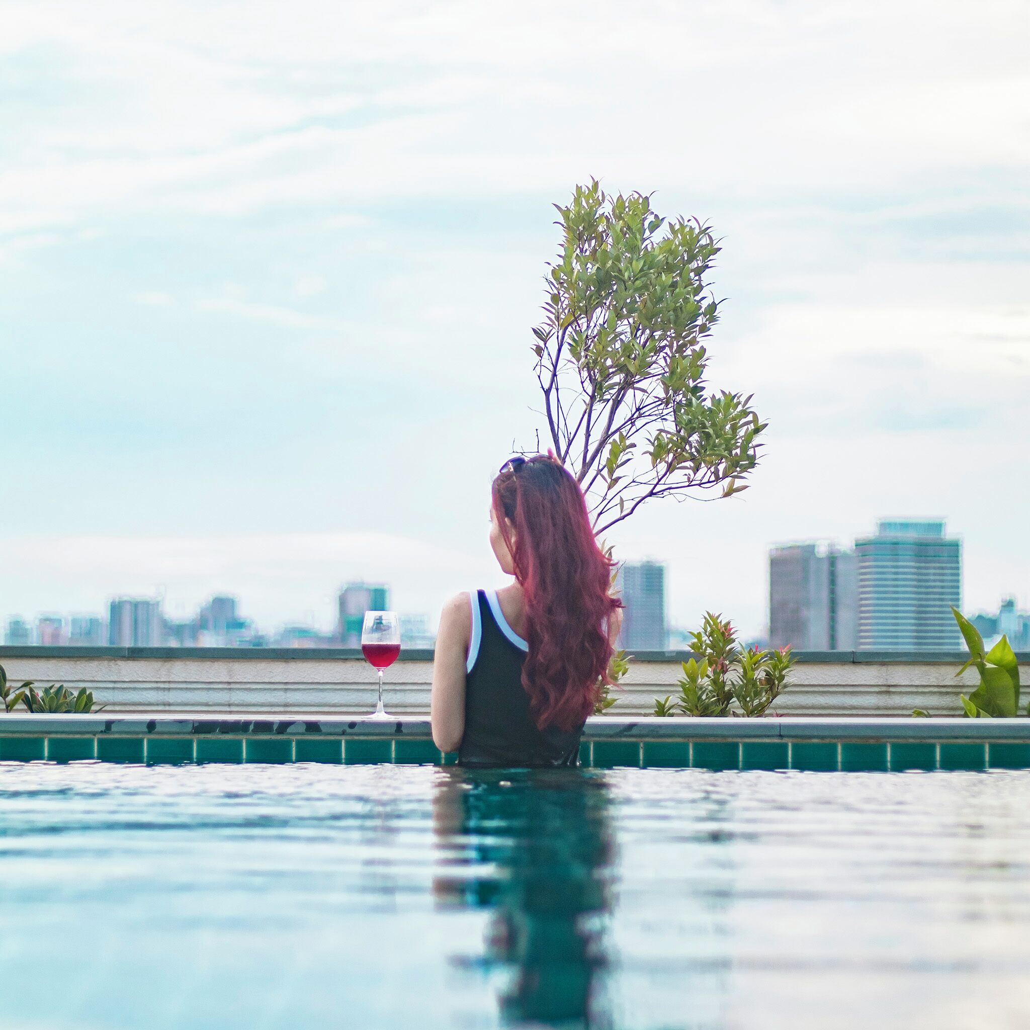 Eine Person sitzt am Pool mit einer Stadtansicht im Hintergrund.