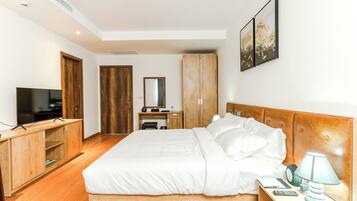 A modern hotel room with a large bed, wooden wardrobe, a desk with a chair, a television, and artwork on the wall.