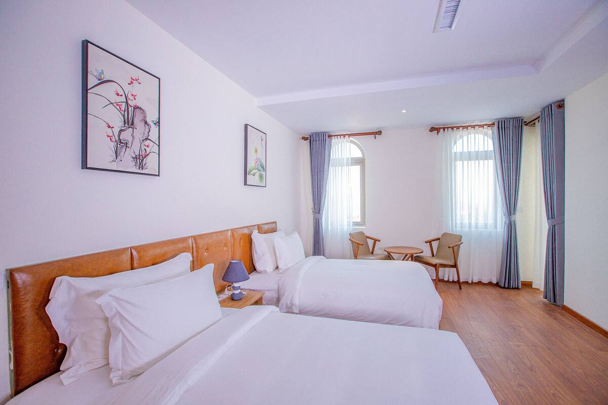 Een hotelkamer met twee bedden, een tafeltje, een stoel en kunstwerken aan de muur.