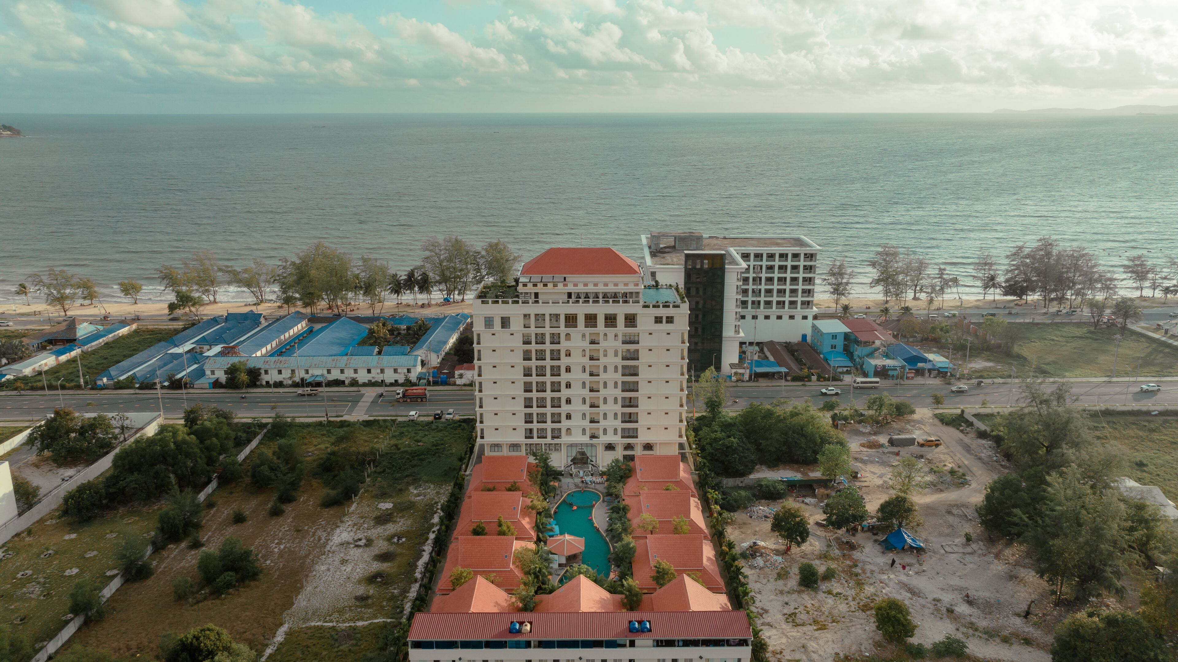 Ett hotell med en central pool, flera byggnader och utsikt över stranden.