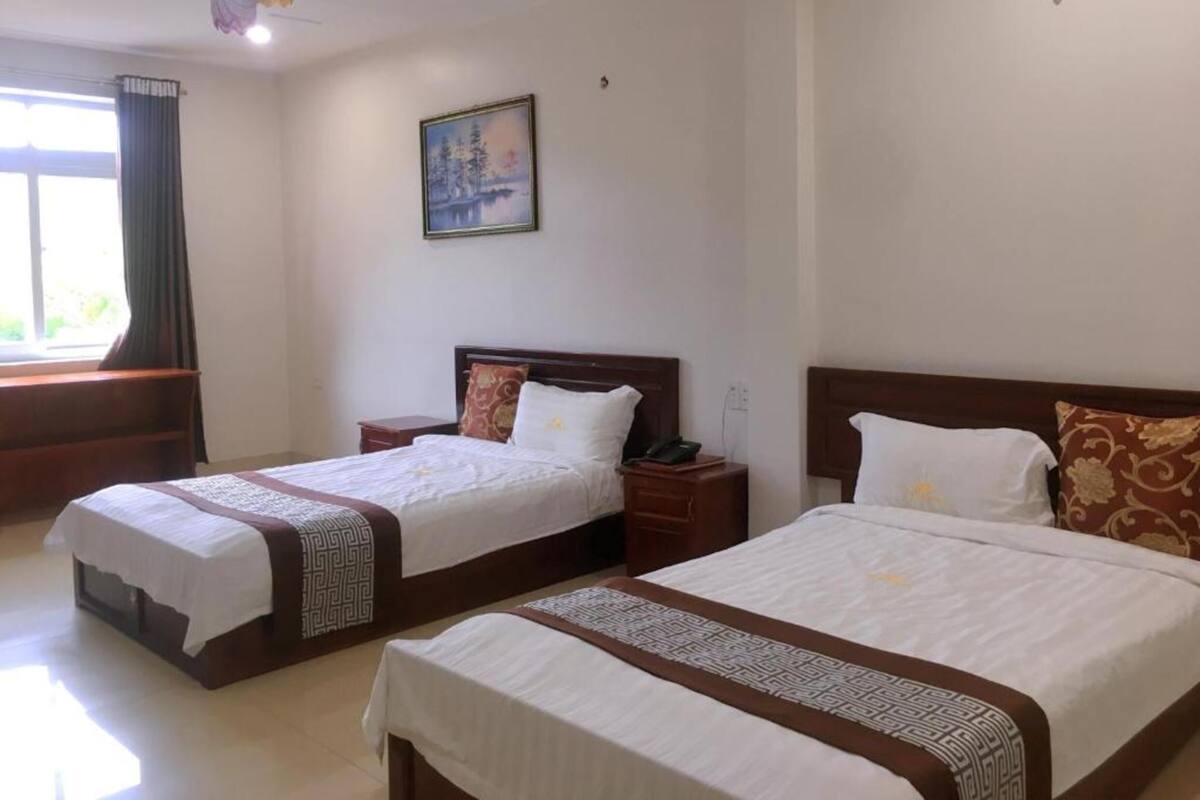 A hotel room with two beds, a painting on the wall, and a window with curtains.