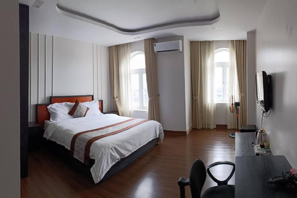 A hotel room with a bed, a desk, a chair, an air conditioning unit, and a TV.