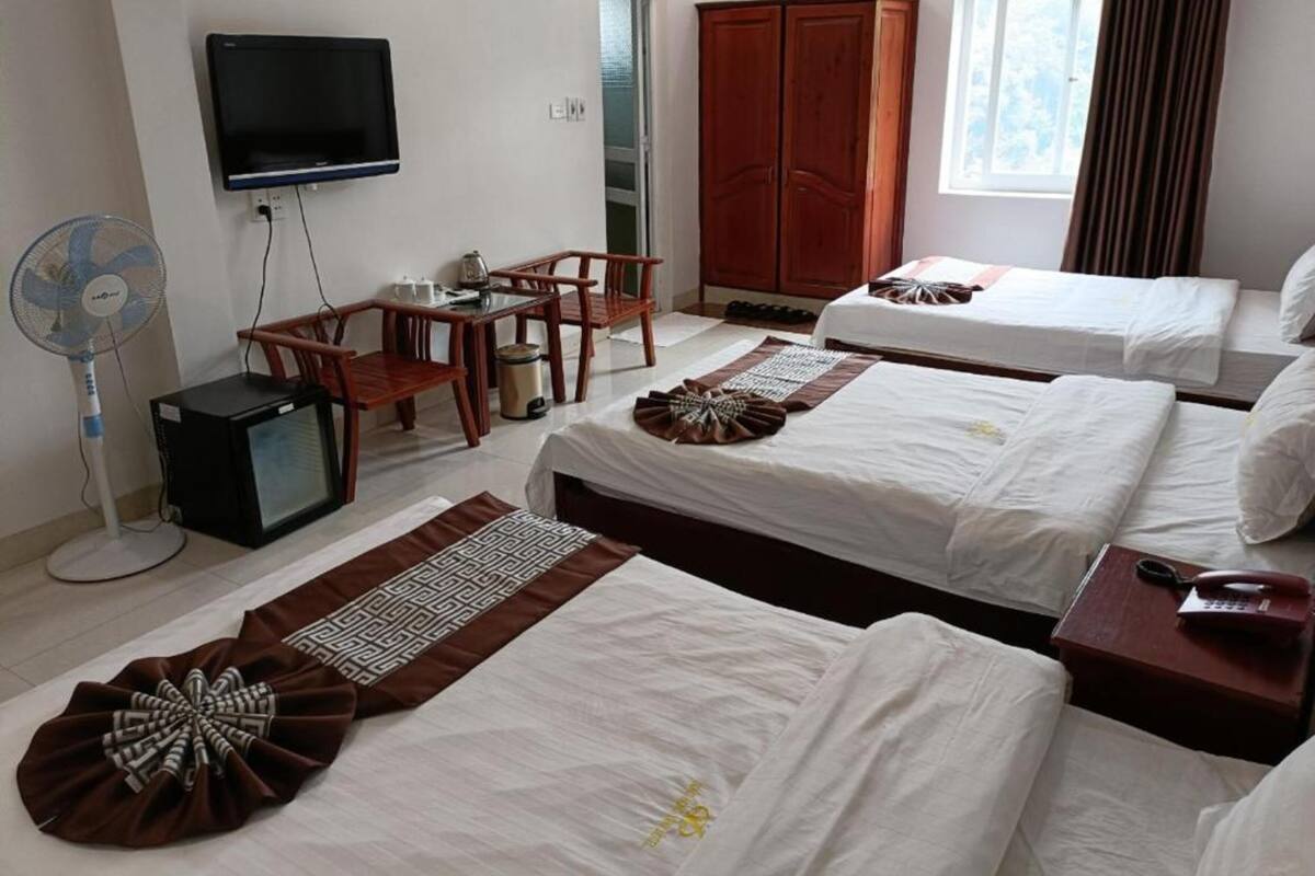 A hotel room with two beds, a TV, a desk with chairs, a wardrobe, and a window with curtains.