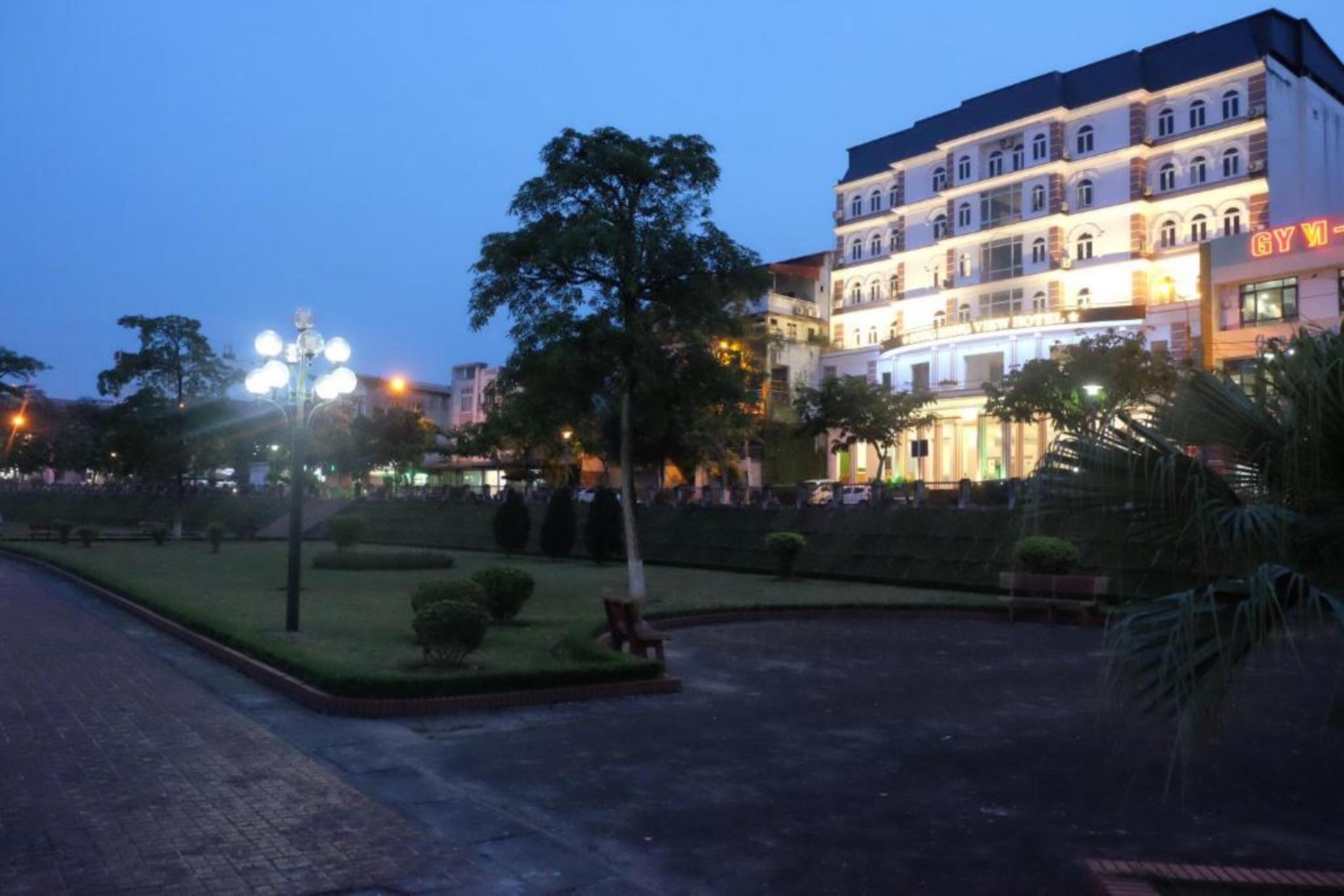 A multi-story hotel with a gym sign, surrounded by a landscaped garden with benches and trees.
