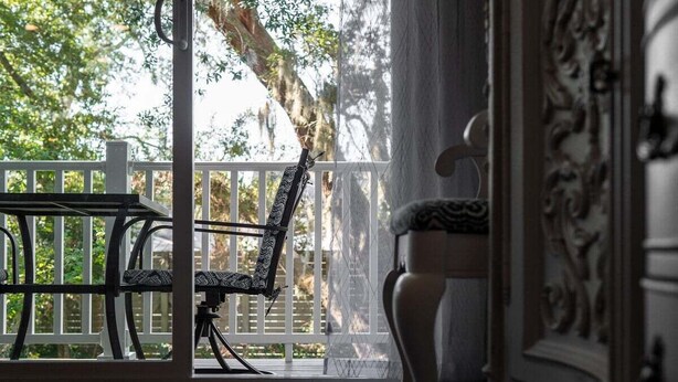 Une véranda avec un banc et une chaise, une balustrade blanche et une vue sur les arbres.