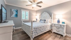 Une chambre à coucher comprenant un lit, des tables de chevet, une commode, un ventilateur de plafond et des œuvres d’art accrochées aux murs.