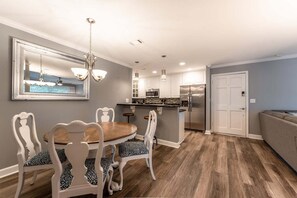 A modern kitchen with white cabinets, a stainless steel refrigerator, and a dining area with a round table and white chairs.