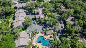 Une vue aérienne d’un quartier résidentiel avec de nombreuses maisons, une piscine centrale et de la végétation luxuriante tout autour.