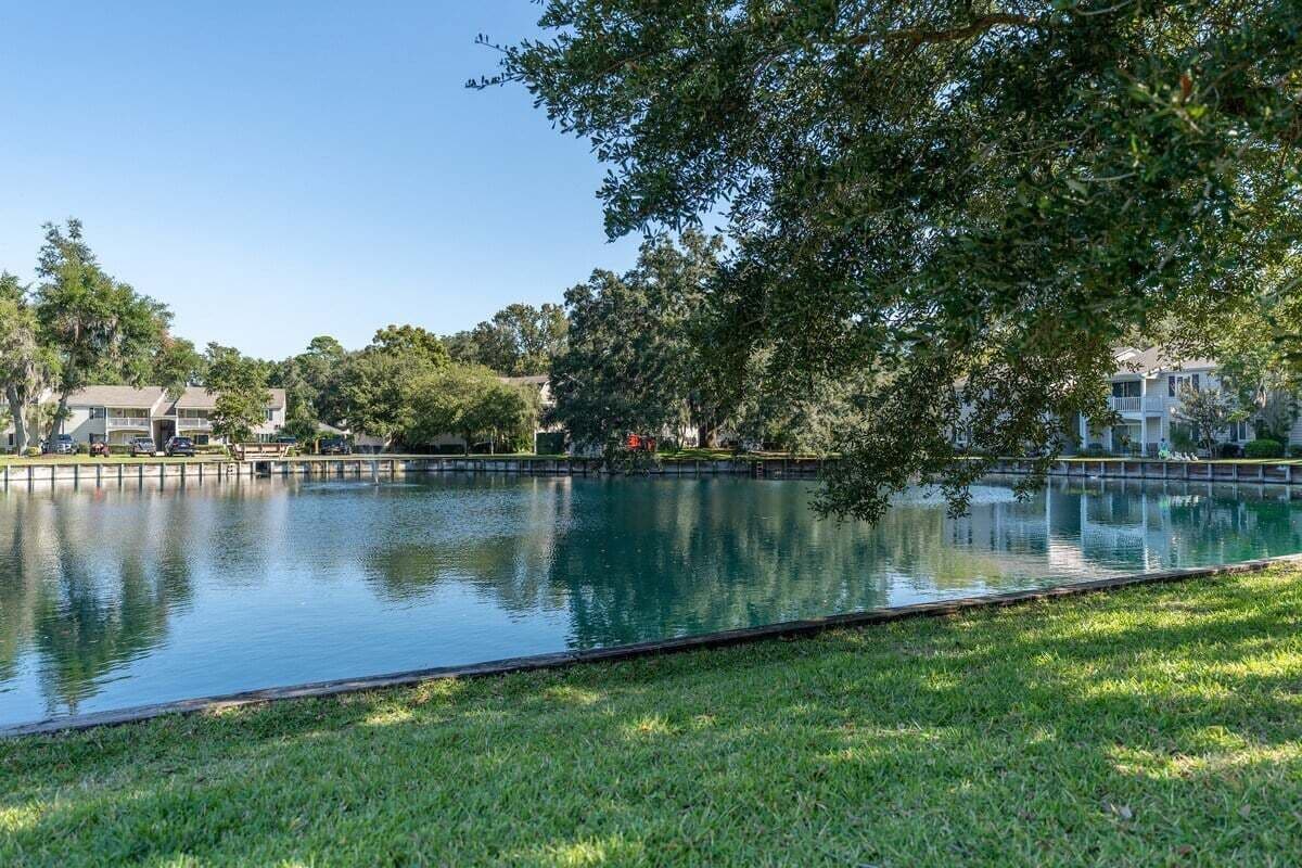 A tranquil outdoor pool area with a grassy foreground, surrounded by trees and residential buildings in the background.
