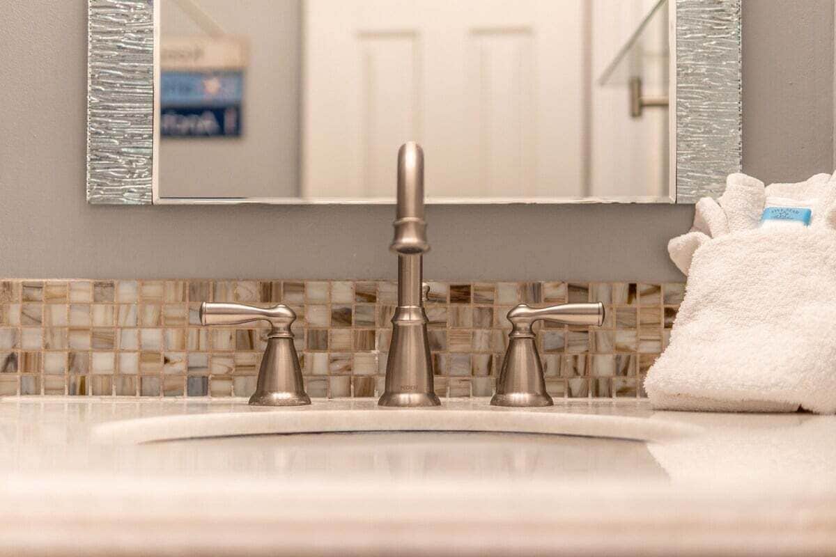 Une salle de bain avec un lavabo, trois robinets, un miroir doté d’un cadre texturé et une serviette blanche.