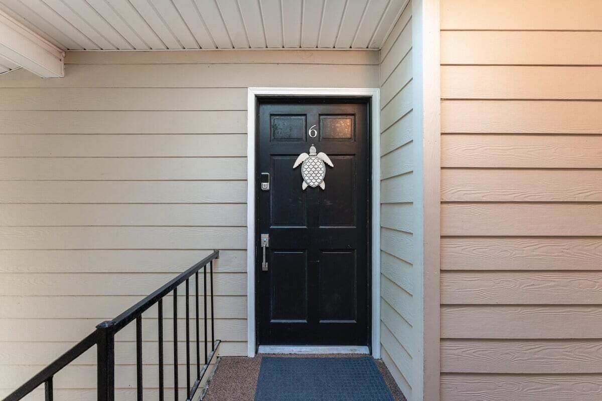 Une porte noire ornée du chiffre « 6 » et d’une décoration représentant une tortue, un garde-corps en métal noir et un revêtement extérieur de couleur beige.
