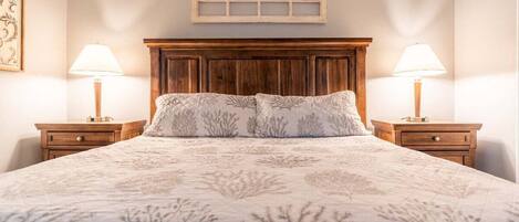Un dormitorio con una cama grande, cabecera de madera, dos mesitas de noche con lámparas y un adorno decorativo sobre la cama.