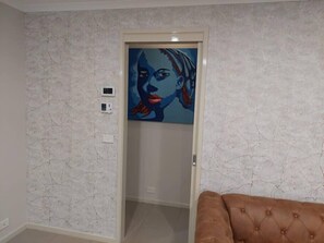 Una habitación con pared blanca texturizada, una obra de arte enmarcada sobre una puerta y un sofá marrón capitonado.