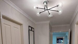 A hallway with a white door, a console table with a plant, a mirror, and a modern chandelier.
