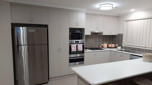 A modern kitchen with stainless steel appliances, grey cabinets, a central island with stools, and a tiled backsplash.
