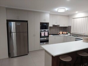 Cocina moderna con electrodomésticos de acero inoxidable, gabinetes grises, una isla central con taburetes y salpicadero de azulejos.