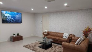 A modern living room with a brown leather sofa, a glass coffee table, and a large flat-screen TV mounted on the wall.