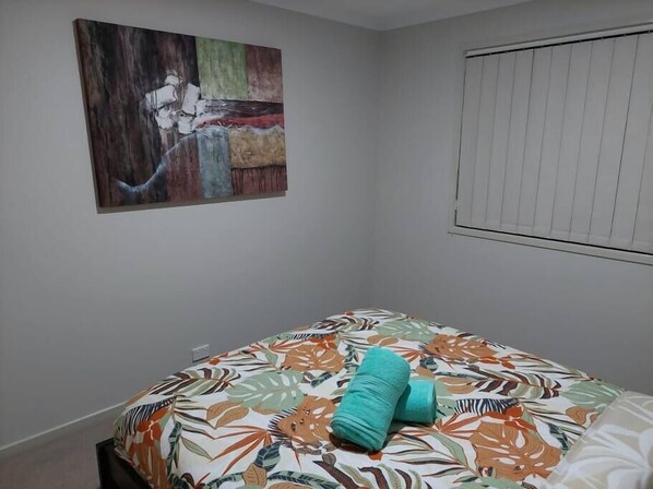 Une chambre à coucher avec un lit, une fenêtre avec des stores et un tableau accroché au mur.