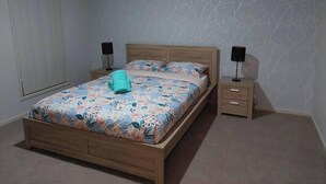 A bedroom with a wooden bed, floral bedding, two bedside tables with lamps, and a plain wall with a tree pattern.