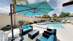 Patio con piscina, muebles de exterior y una sombrilla grande.