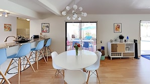 Una cocina moderna con una isla central, taburetes azules, una mesa de comedor blanca y un candelabro.