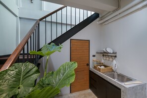 A modern kitchen with a wooden door, a sink, and a staircase with a black railing.