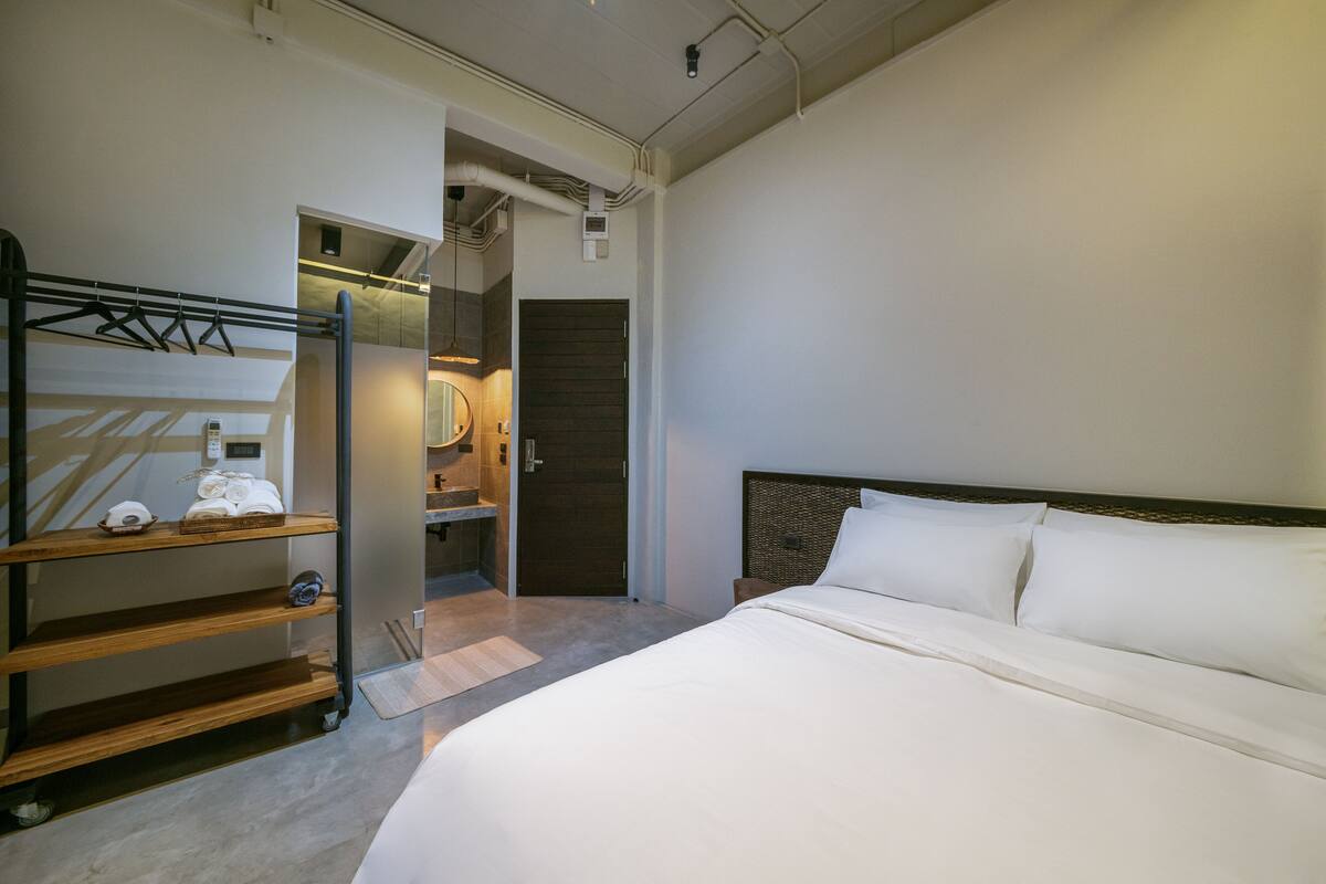 Een hotelkamer met een groot bed, een kast met planken, een spiegel en een deur naar een badkamer.