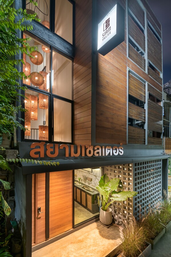 A modern building with a wooden facade, a sign reading "Siam Shelter," and a potted plant outside.