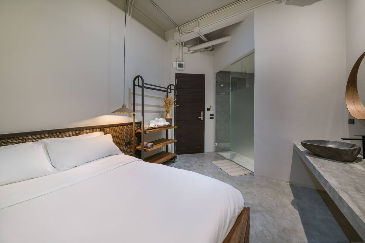 Een moderne hotelkamer met een groot bed, een houten nachtkastje, een douchecabine van glas en een ronde spiegel op de wastafel.