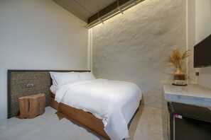 A modern bedroom with a wooden headboard, a single bed, a small wooden stool, a nightstand, and a flat-screen TV on a marble countertop.
