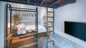 A modern room with a bed, a bench, a TV, a shelf with towels, a vase, and a mirror.