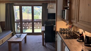 Een gezellige woonkamer met een bank, een salontafel en een televisie. Er is een balkon met uitzicht op het platteland.