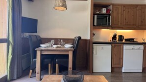 Een eetruimte met een tafel voor vier personen, een keuken met houten keukenkastjes, een magnetron en een vaatwasser.
