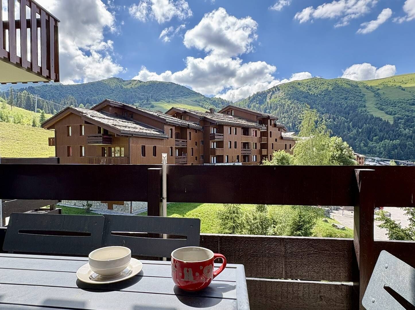 A table with a bowl and a mug, overlooking a mountain landscape with buildings.