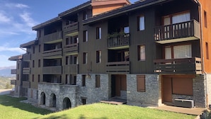 A multi-story building with balconies, stone base, and a grassy area in front.