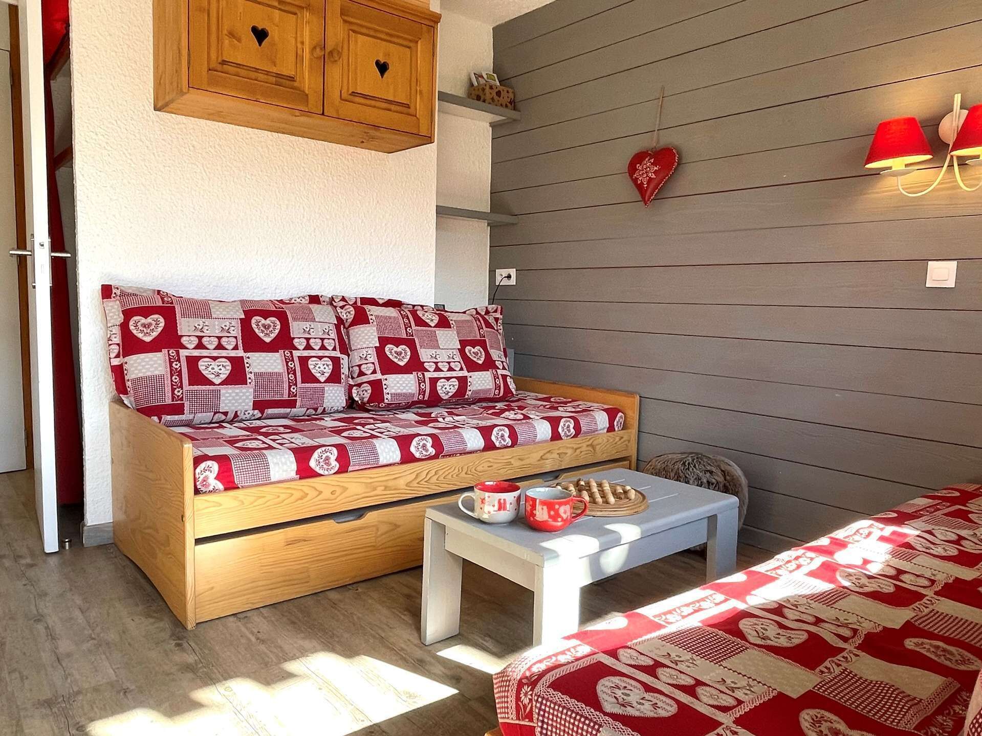 A cozy room with a wooden sofa bed, a small white table, and a red heart-shaped decoration on the wall.