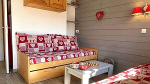 A cozy room with a wooden sofa bed, a small white table, and a red heart-shaped decoration on the wall.