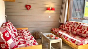 A cozy room with a wooden wall, a red heart decoration, two red lamps, and a window with curtains.