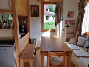 A compact room with a wooden table, a sofa, a radiator, and a window with curtains.