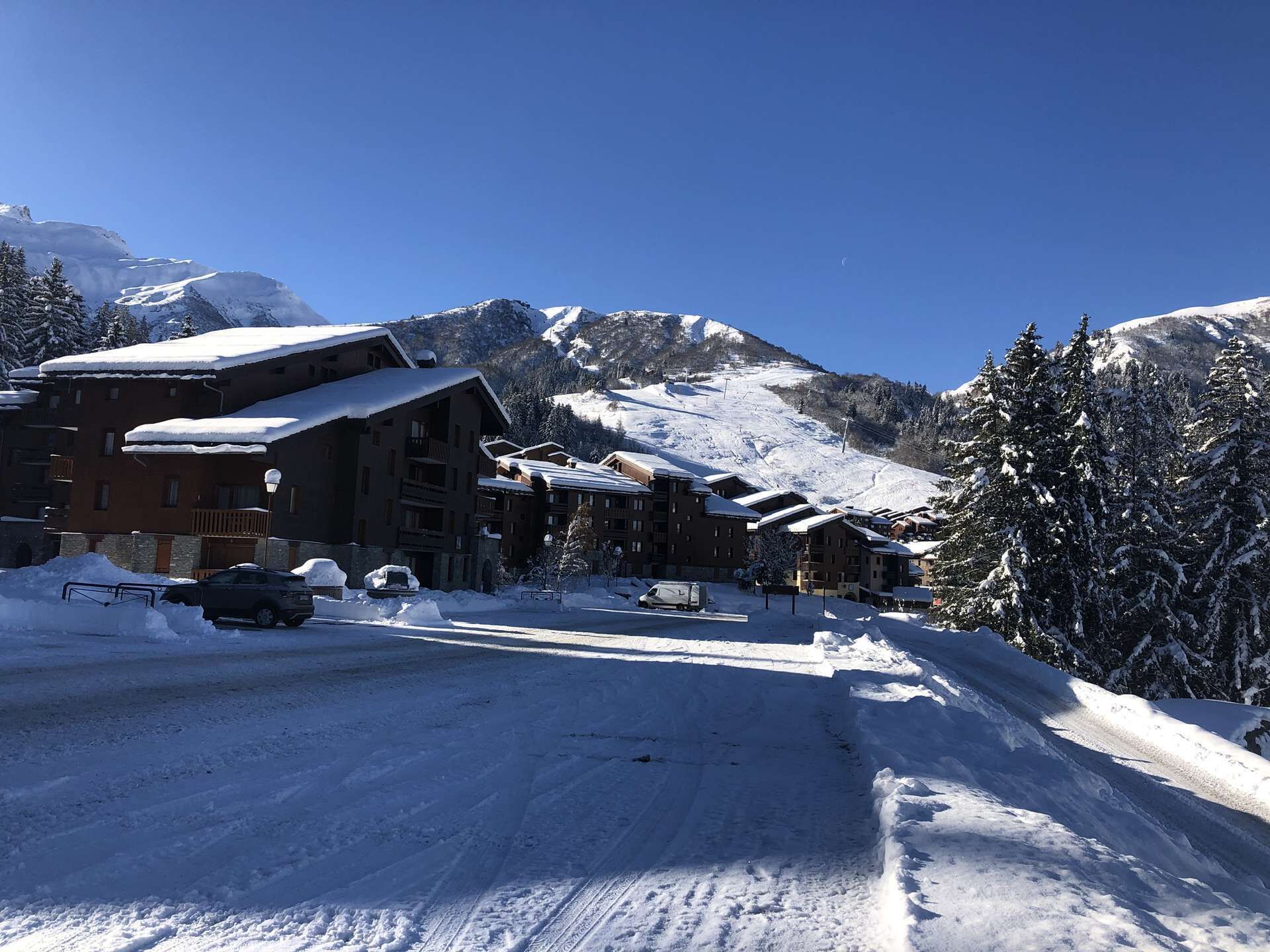 A snow-covered mountain resort with chalet-style buildings, a clear sky, and a ski slope in the background.