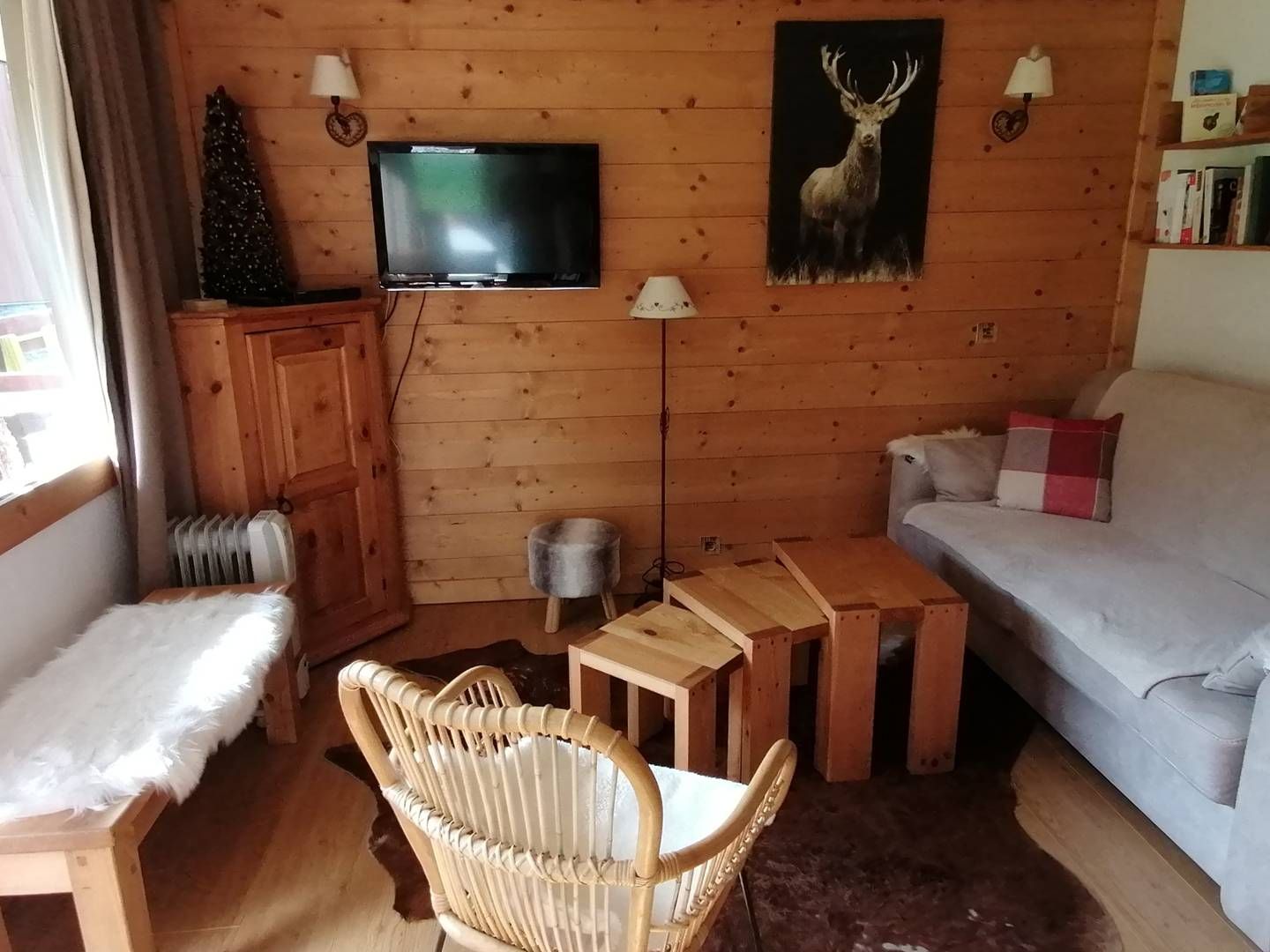 Una sala de estar acogedora tipo cabaña, con un televisor, un sofá, una silla, una mesita y un árbol de Navidad.