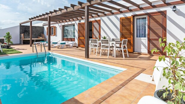 A poolside area with a pergola, outdoor seating, and a stone wall. - Villa Vela Private Pool Playa Blanca Pool Playa Blanca (Playa Blanca)