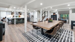 Une cuisine spacieuse et moderne, dotée de meubles blancs et d’un îlot central, qui s’ouvre sur un coin repas avec une grande table et des chaises en bois.