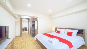 Een hotelkamer met een groot bed, een houten hoofdbord en een rode accent loper. Links staat een televisie en in de hoek een houten kast.