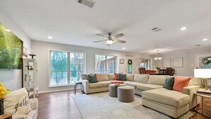 A spacious living room with a large sectional sofa, a ceiling fan, and large windows providing natural light.