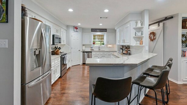 A modern kitchen with white cabinetry, stainless steel appliances, and a marble countertop.