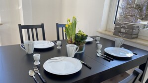 Ett matbord dukat med vita tallrikar, koppar och bestick, en krukväxt med gula blommor och ett fönster med utsikt över träd.