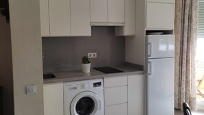A compact kitchen with a built-in washing machine, a refrigerator, and a small countertop with a potted plant. - Studio with terrace and spectacular views (La Línea de la Concepción)