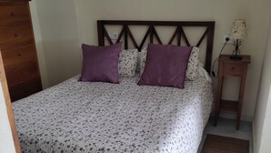 A neatly made bed with a floral-patterned bedspread, two purple pillows, and a headboard with a wooden frame. - Studio with terrace and spectacular views (La Línea de la Concepción)