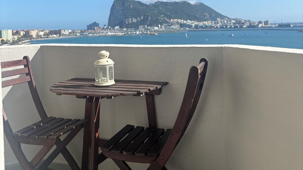 A balcony with a table and chairs, overlooking a coastal cityscape with a prominent mountain. - Studio with terrace and spectacular views (La Línea de la Concepción)